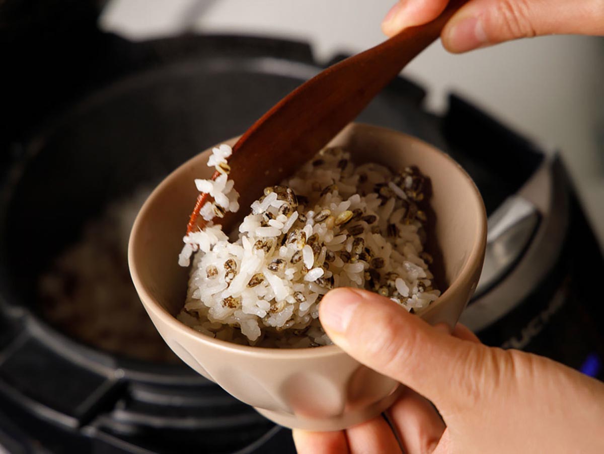 쌀과 검은쌀이 섞인 밥을 공기그릇에 주걱으로 담고 있다.