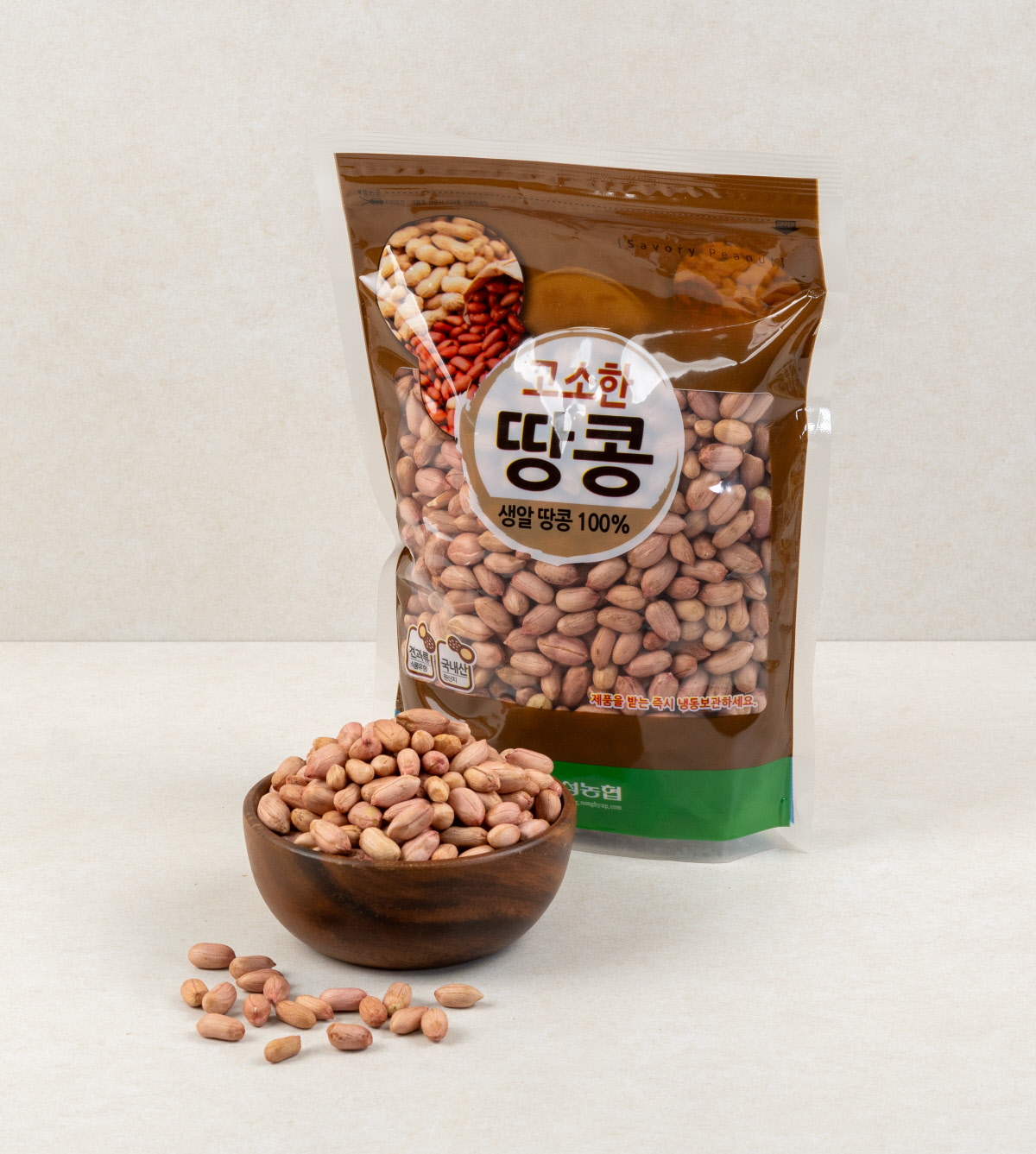 생알땅콩 100% 문구가 적힌 갈색 포장과 함께 그릇에 담긴 국산 생땅콩이 놓여 있는 장면으로, 1kg 포장 상태와 알땅콩의 실물을 함께 보여줌.