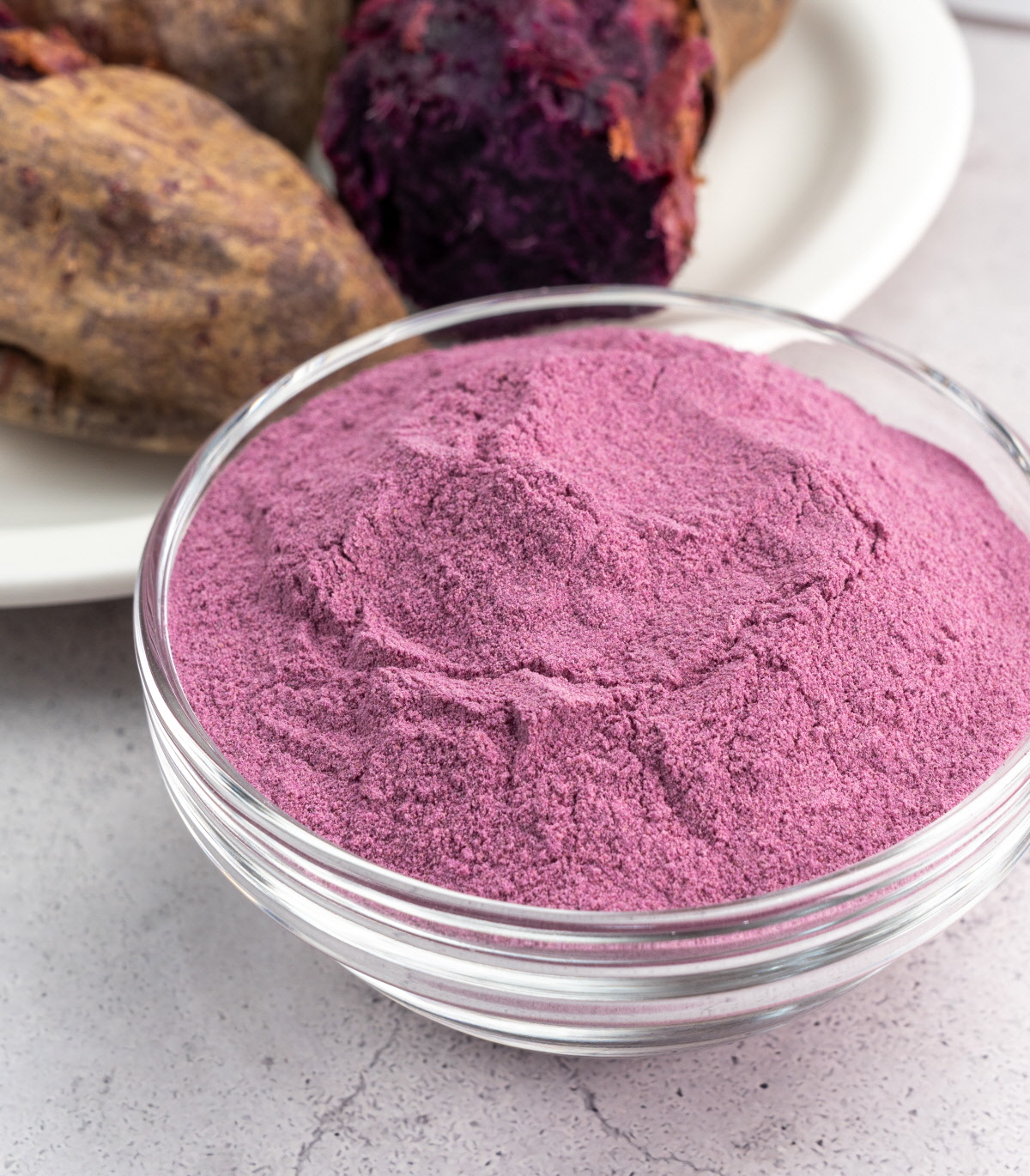 국산자색고구마를 구워 곱게 갈아 만든 고운 보라색 고구마분말이 투명한 유리볼에 담긴 모습, 뒤쪽에는 구운 자색고구마 단면이 보이는 구도