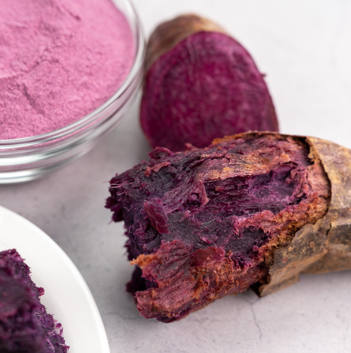 구운 자색고구마와 자색고구마분말이 함께 놓인 구도, 고구마 껍질의 구운 질감과 속의 진한 보라색이 대조를 이루는 모습