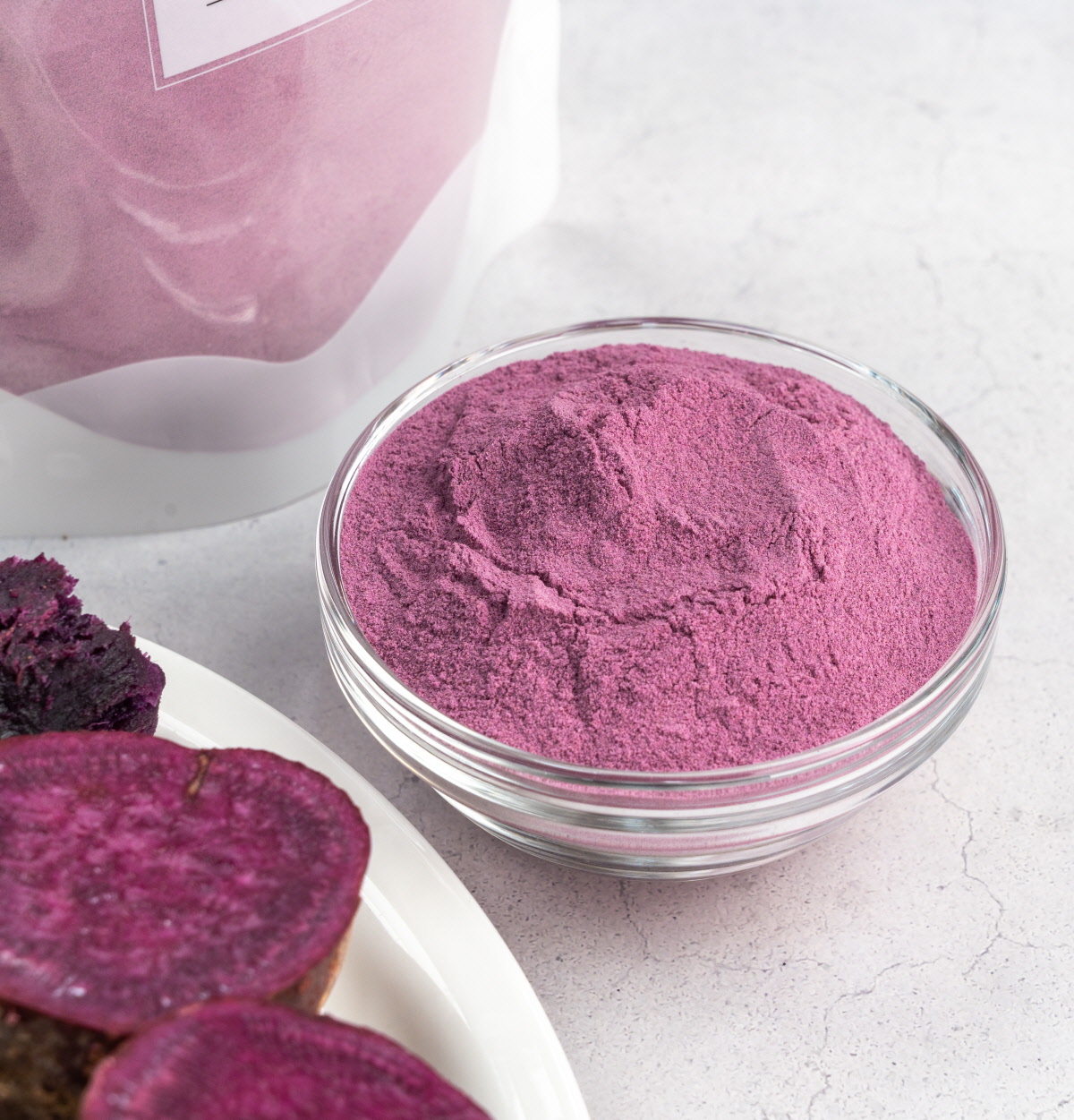 보라고구마로 만든 고운 자색고구마분말이 유리볼에 담겨 있고, 옆에는 구운 고구마 단면이 진한 자색빛을 띠며 놓여 있는 장면