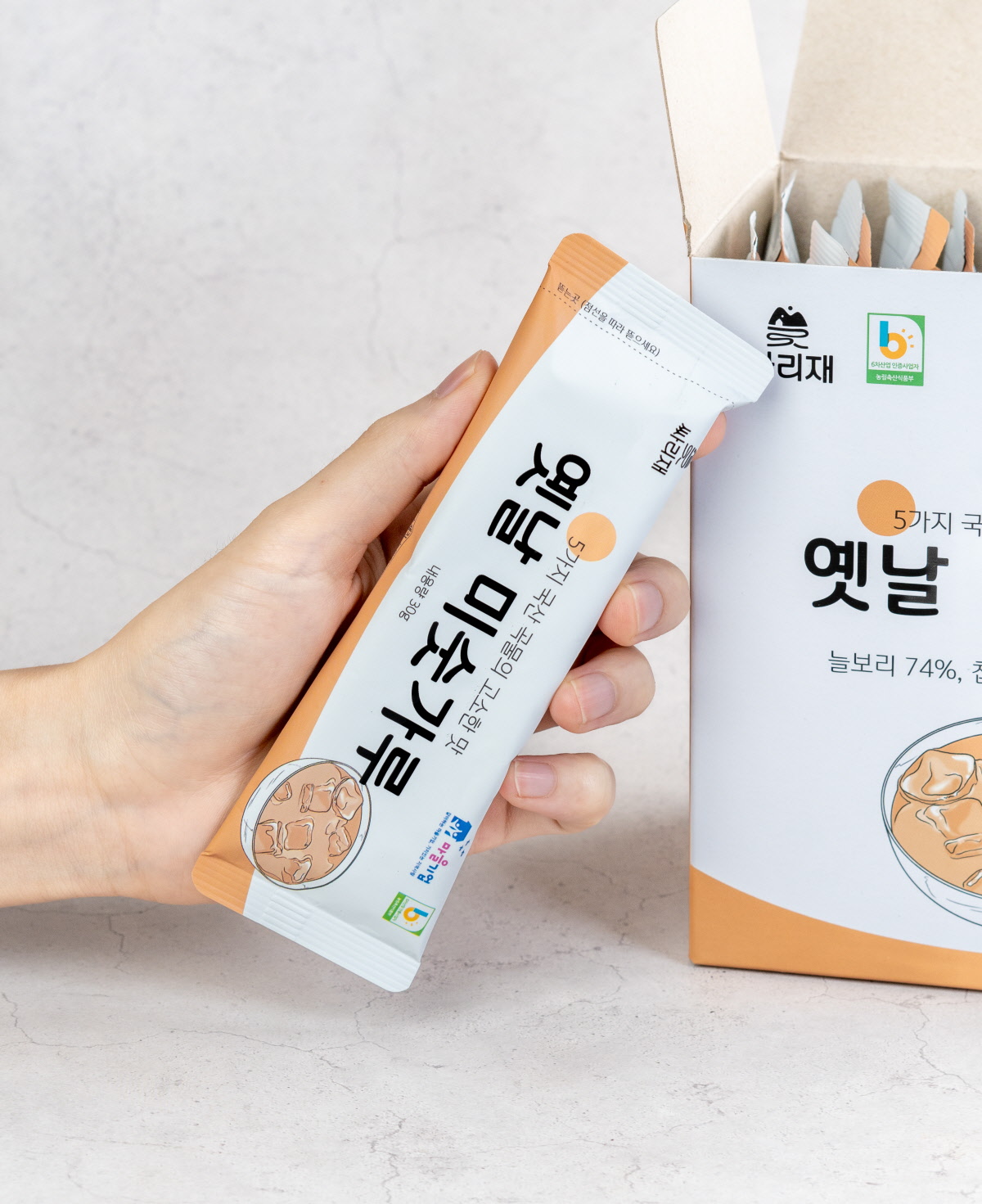 한 손에 들기 좋은 개별포장 미숫가루 스틱을 클로즈업한 모습. 간편하게 휴대하며 하루콩력 채우는 아침대용식으로 적합한 디자인.