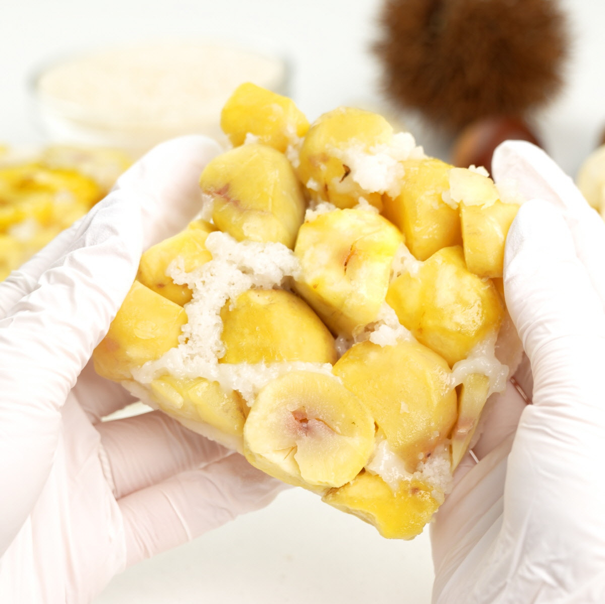 자연해동 아침대용 밤설기 조각을 장갑 낀 손으로 들어 올려 알밤 알갱이와 촉촉한 설기층이 가까이에서 보이도록 강조