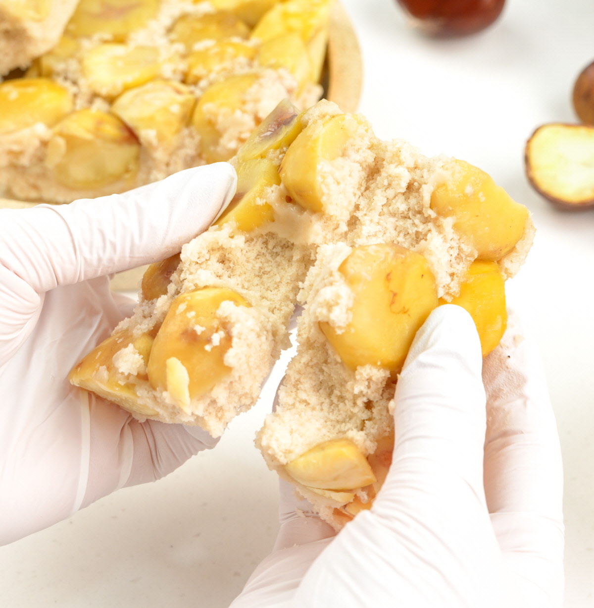 양손으로 밤설기 조각을 갈라 속살의 고운 쌀가루층과 촉촉한 밤 알갱이가 드러나는 장면으로, 설기떡의 부드러운 결을 강조함