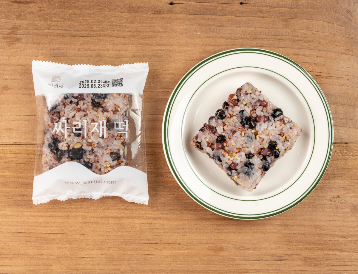 간편 영양식 오곡밥 담음새 흰 접시 위에 네모 모양 잡곡밥이 놓이고 옆에 싸리재 떡 문구가 보이는 개별포장이 함께 배치된 상단 구도