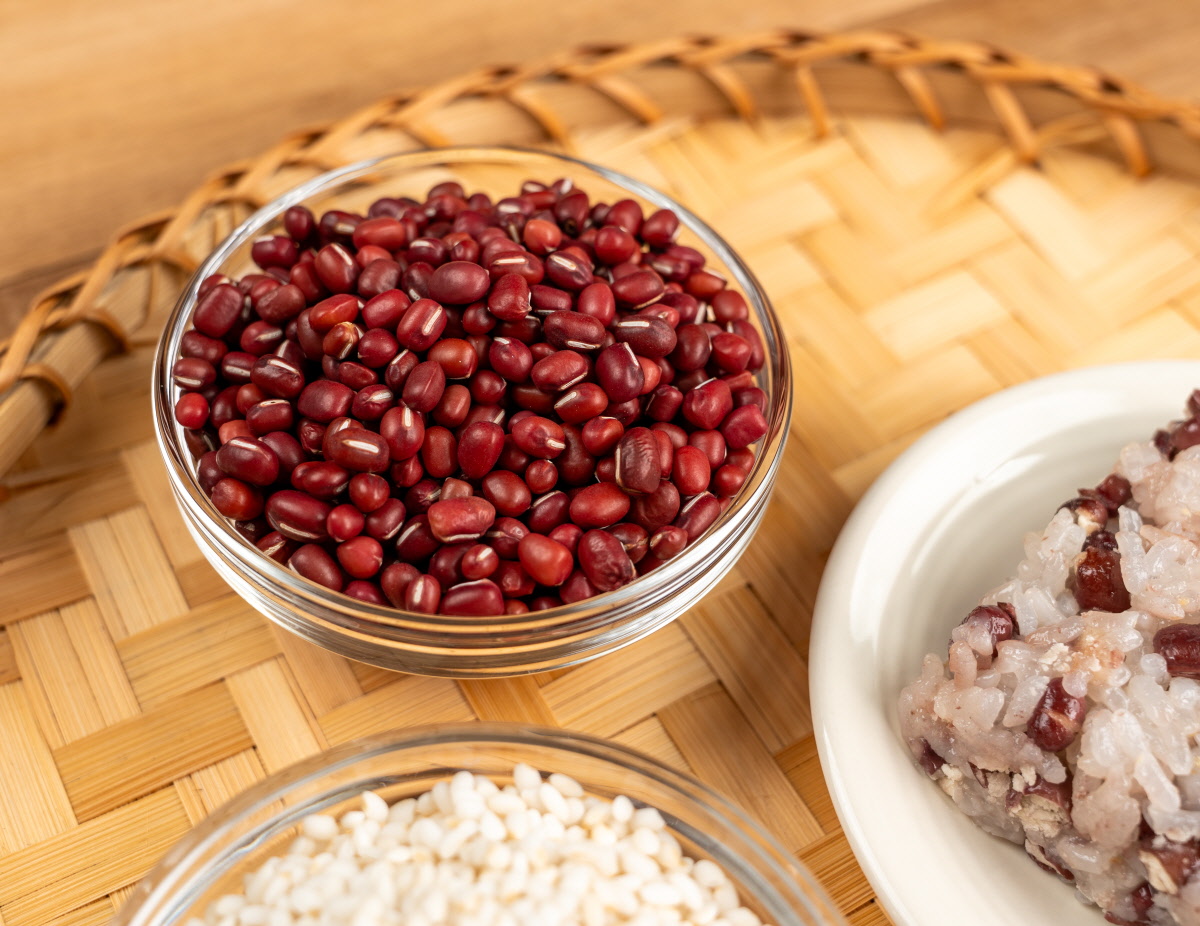 유리 볼에 담긴 선명한 붉은색의 국산 팥과 갓 쪄낸 팥 찰밥의 대비 컷