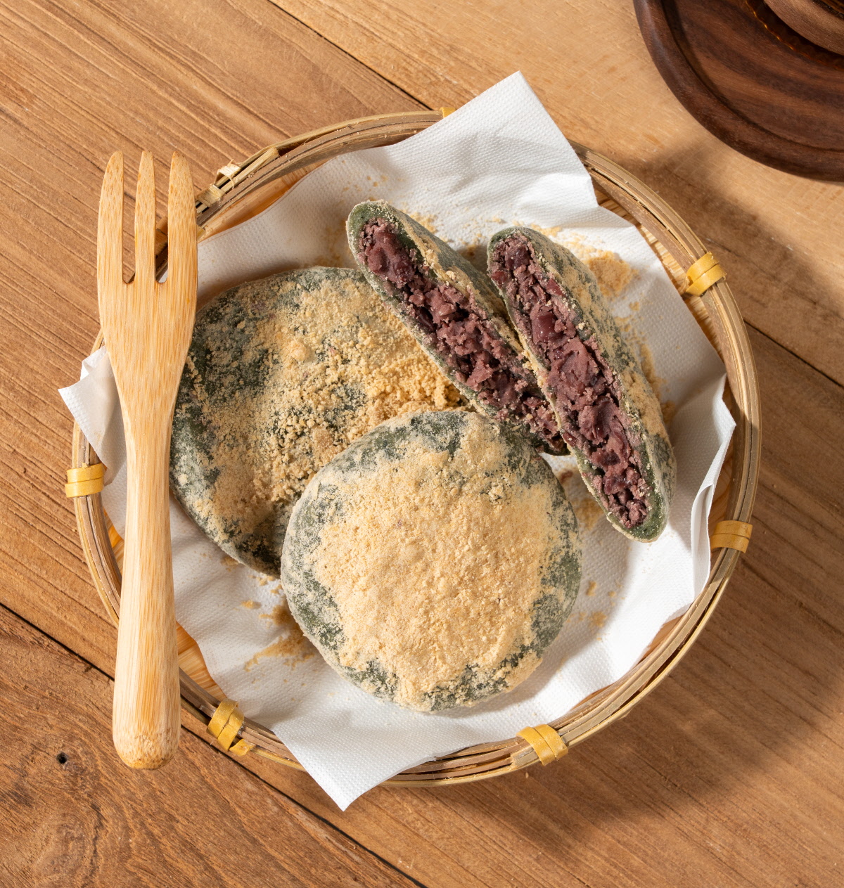 앙금쑥개떡 싸리재 개떡을 둥근 채반에 담아 위에서 내려다본 모습으로 콩고물 묻은 떡 두 개와 반으로 가른 통팥앙금 단면 두 조각이 함께 놓여 있는 구성