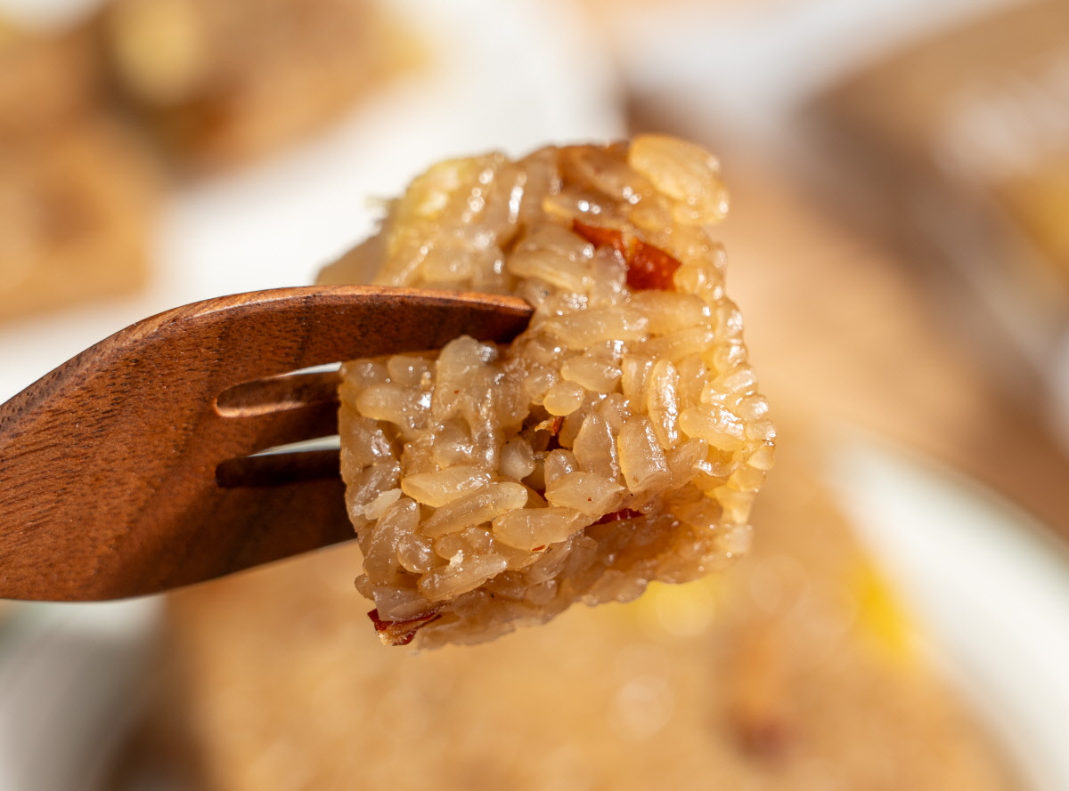 약밥 아침대용으로 한입 집어 먹는 장면으로 나무 포크 끝에 윤기 도는 찹쌀알이 뭉쳐 있고 속에 대추 조각과 밤 조각이 보이는 모습