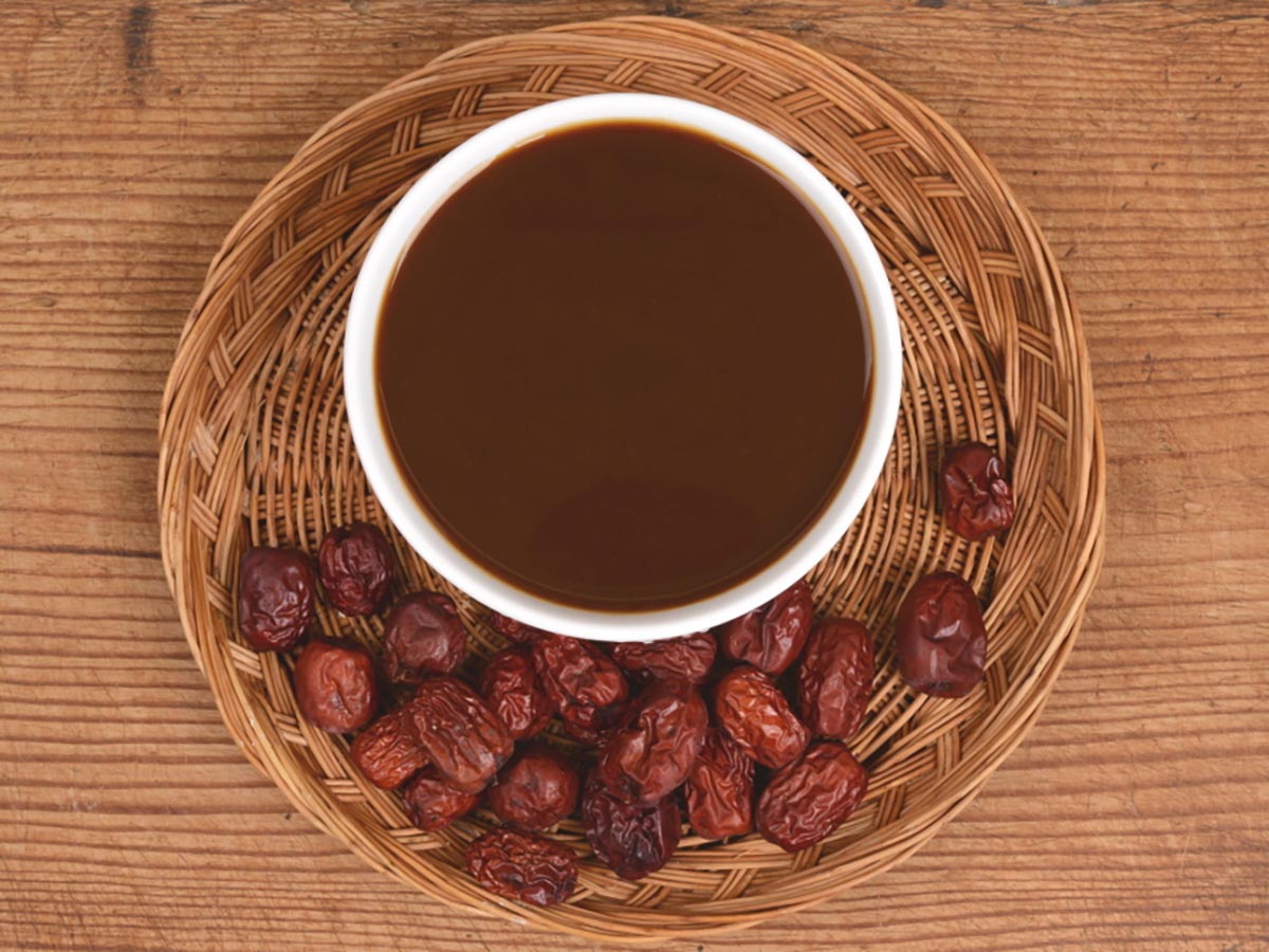 출출할때 간편식 약밥에 넣는 대추고가 짙은 갈색으로 그릇에 담겨 있고 라탄 트레이 위에 윤기 도는 대추고 표면이 매끈하게 보이며 주변에 말린 대추가 함께 놓인 모습
