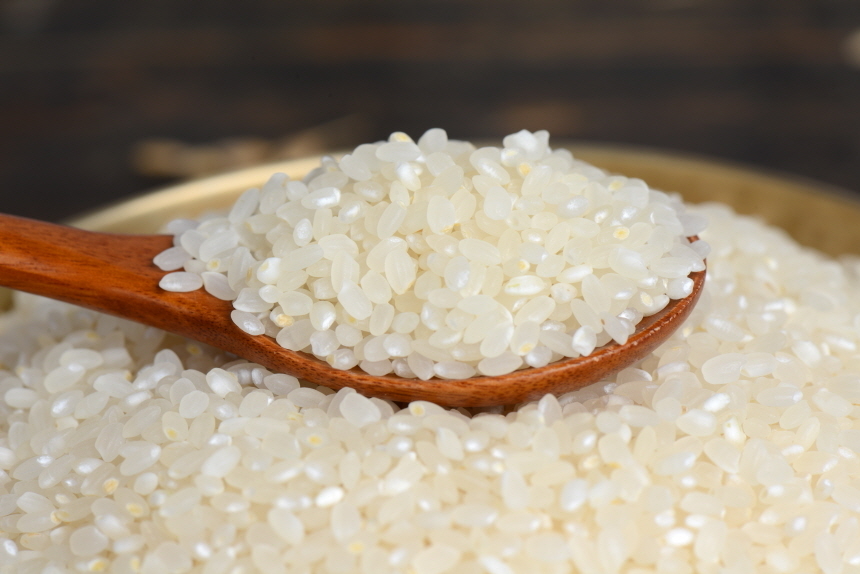 금색 둥근 놋그릇에 하얀 백미쌀알들이 수북이 쌓여있고, 이 쌀알을 나무숟가락으로 가득 퍼올린 모습입니다.