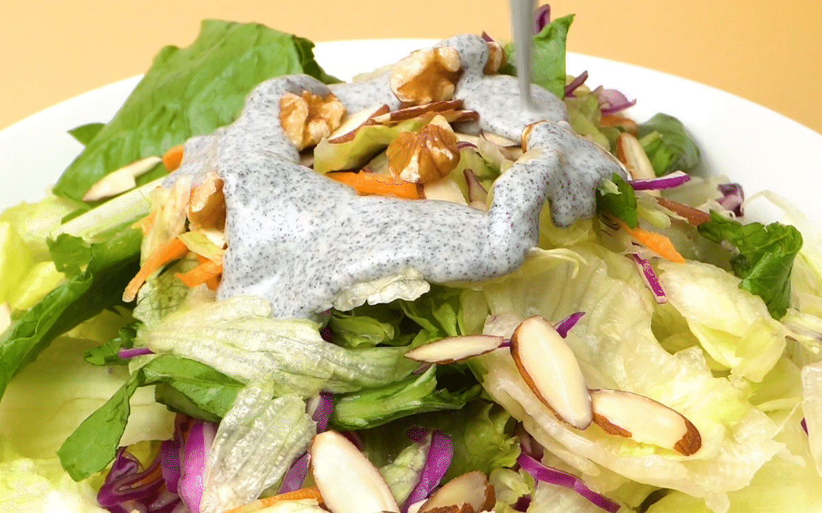 흑임자가루로 만든 드레싱이 샐러드 위에 부드럽게 흘러내리며, 채소와 견과류 사이로 고소한흑임자와 볶은깨 향이 어우러진 장면.