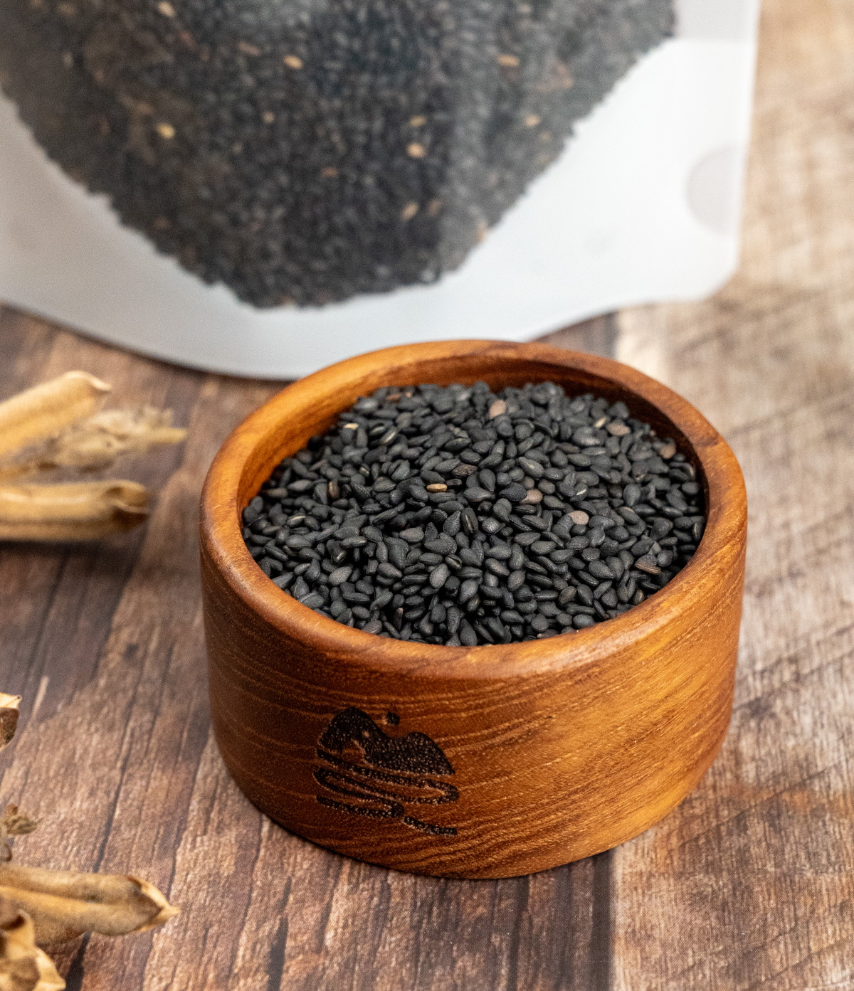 국산흑임자가 작은 나무 그릇에 가득 담겨 있으며, 자연스러운 나무 결과 싸리재 로고가 새겨진 그릇이 흑임자가루 원료의 고급스러움을 살려주는 장면.