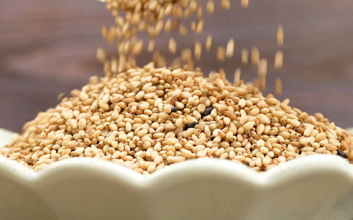 볶은참깨가 그릇 위로 부드럽게 떨어지며 쌓이는 장면으로, 국산참깨 특유의 고소한 향과 통참깨의 윤기 있는 질감이 자연스럽게 표현됨.