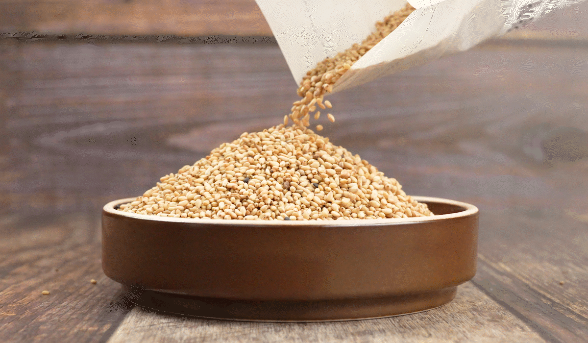 지퍼백 포장에서 볶은참깨가 갈색 접시로 부드럽게 쏟아져 쌓이고 있으며, 고소한참깨 특유의 노르스름한 색감과 국산참깨 알갱이가 살아 있는 장면.