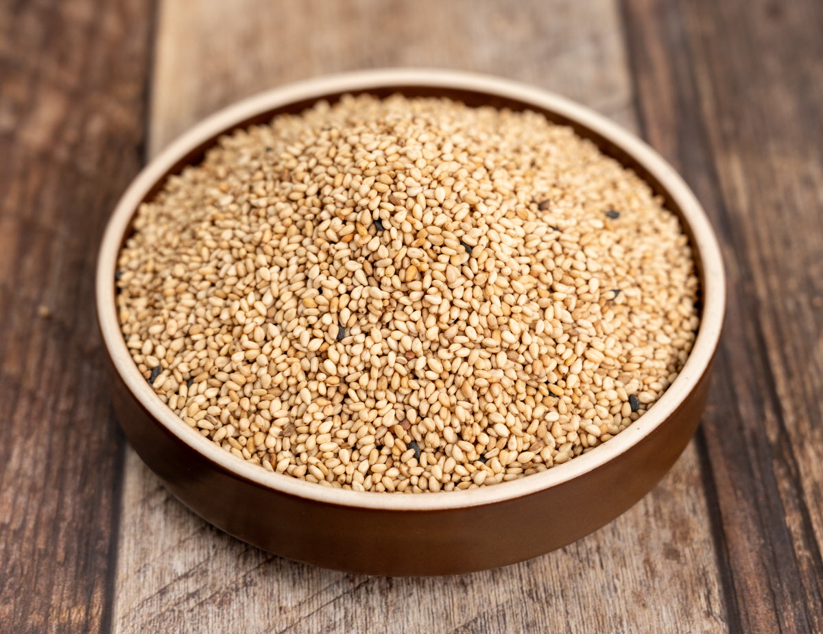 나무 느낌의 갈색 접시에 볶은참깨와 고소한참깨가 수북이 담겨 있고, 국산참깨 알갱이가 골고루 섞여 고명이나 요리토핑참깨로 쓰기 좋은 풍성한 양을 보여주는 장면.