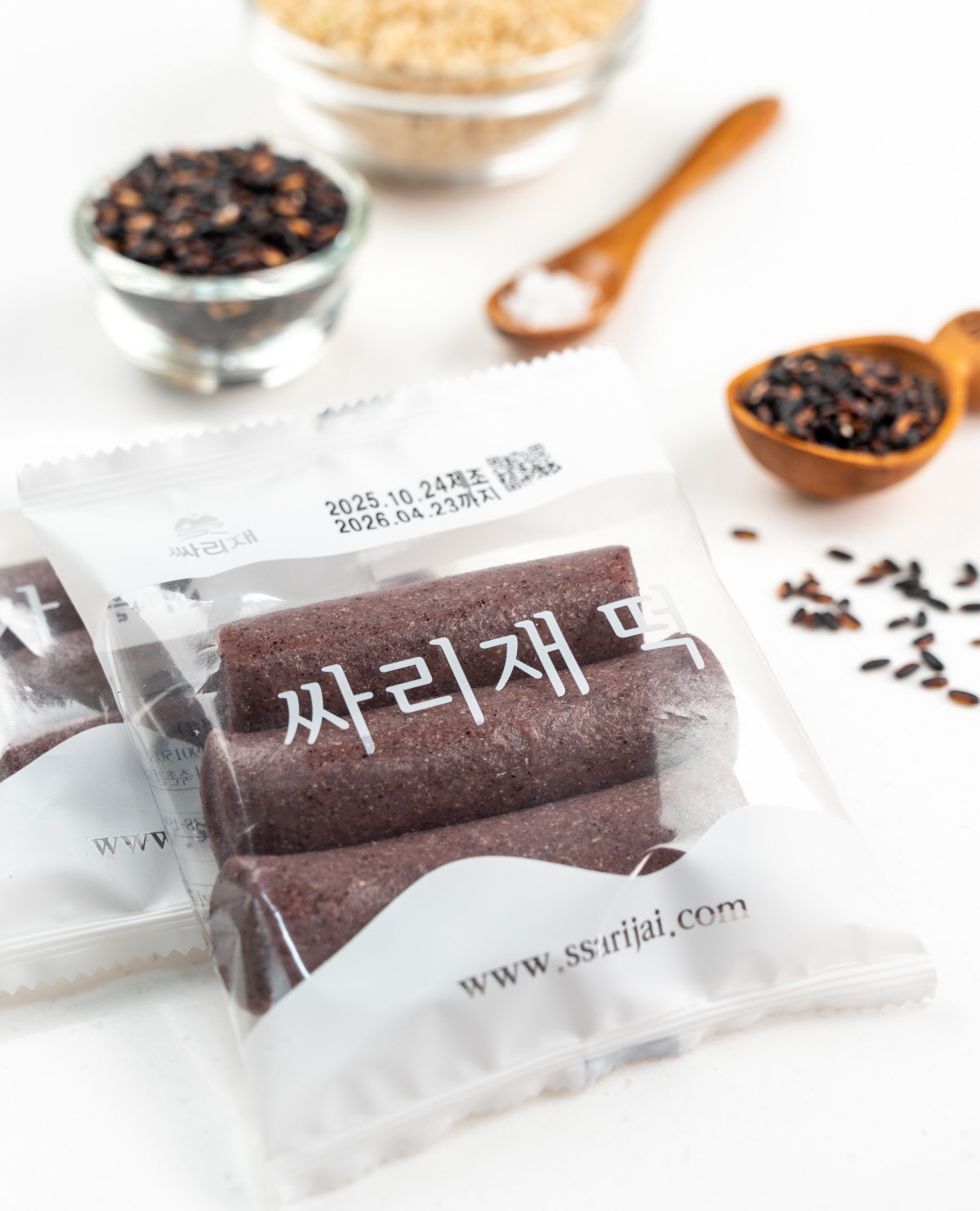 흑미떡을 포크로 들어 꿀에 찍은 장면으로, 쫀득한 가래떡의 질감과 윤기 나는 단면이 고소한 현미떡의 맛을 돋보이게 한다. 달지 않은 건강간식으로 아침대용떡이나 간식으로 즐기기 좋다.