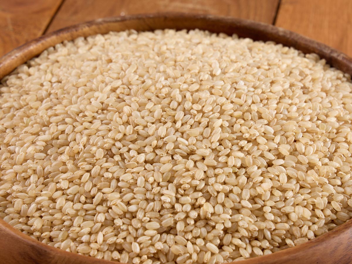그릇에 찹쌀, 흑미, 현미쌀이 수북히 담아져 있고, 현미쌀이 손바닥 위에 올려져 있다.