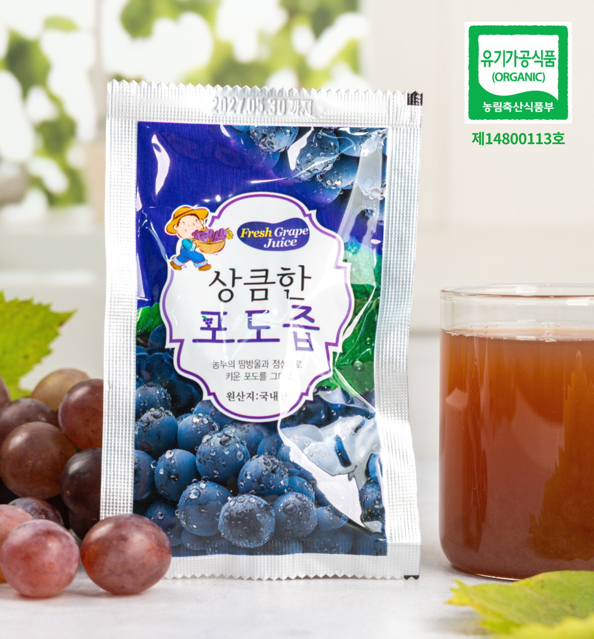 상큼한 포도즙 파우치와 컵 ‘상큼한 포도즙’ 문구가 적힌 파우치가 포도알과 함께 서 있고, 옆의 잔에는 유기농포도즙 특유의 갈색빛 포도착즙이 담겨 있는 모습.