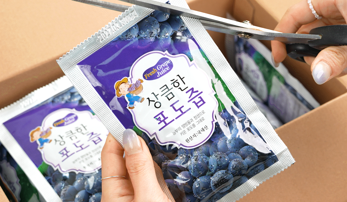 포도즙 파우치 개봉 장면 박스에서 유기농포도즙 파우치를 꺼내 가위로 윗부분을 자르는 모습으로, ‘상큼한 포도즙’ 문구가 선명해 한 봉씩 간편하게 여는 국산포도즙임을 보여준다.