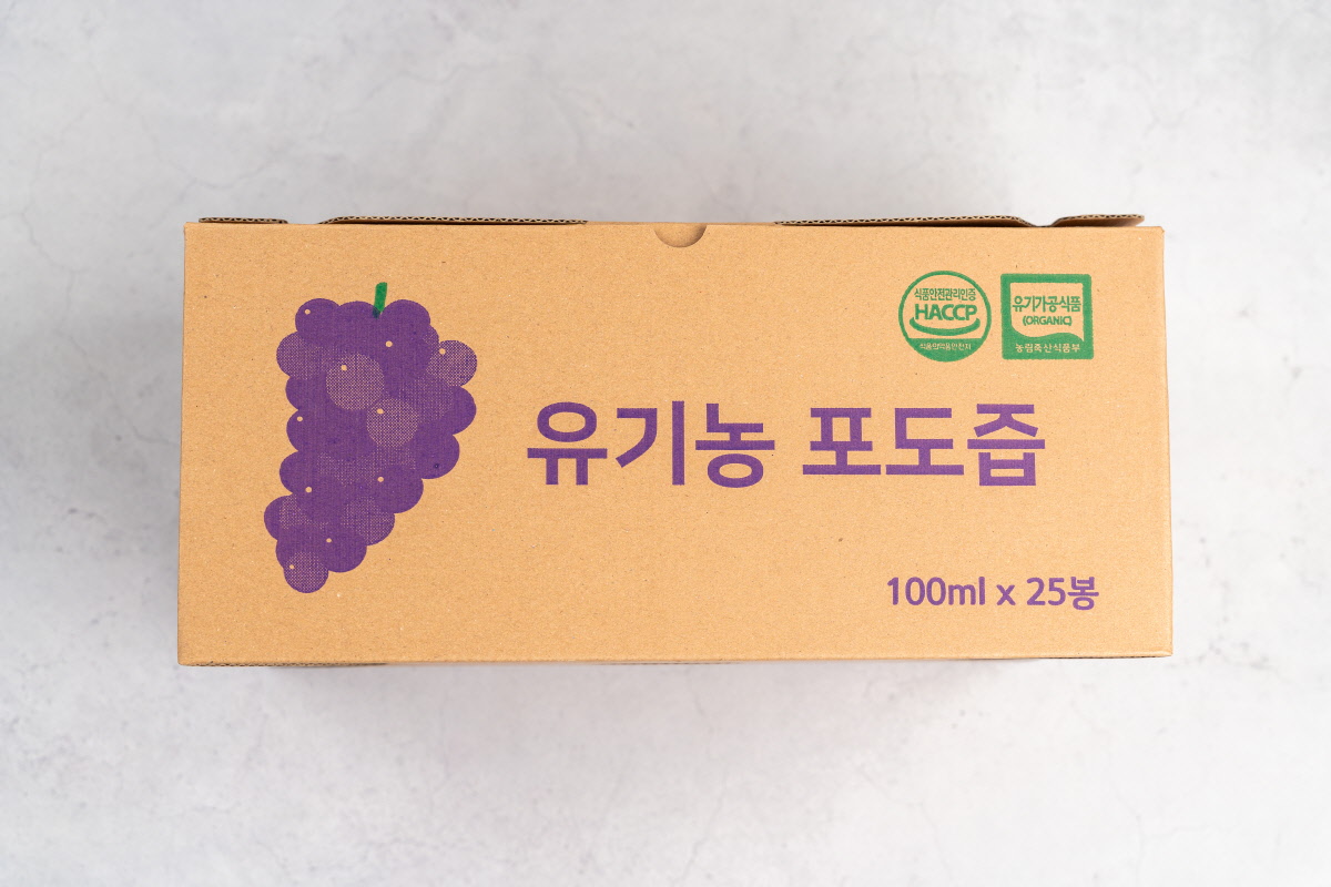 유기농포도즙 25봉 선물박스 정면 앞면에 보라색 포도 일러스트와 함께 ‘유기농 포도즙 100ml x 25봉’ 문구, HACCP와 유기농 인증 마크가 인쇄된 박스가 놓여 있어 유기농포도즙 선물용 패키지를 보여준다.
