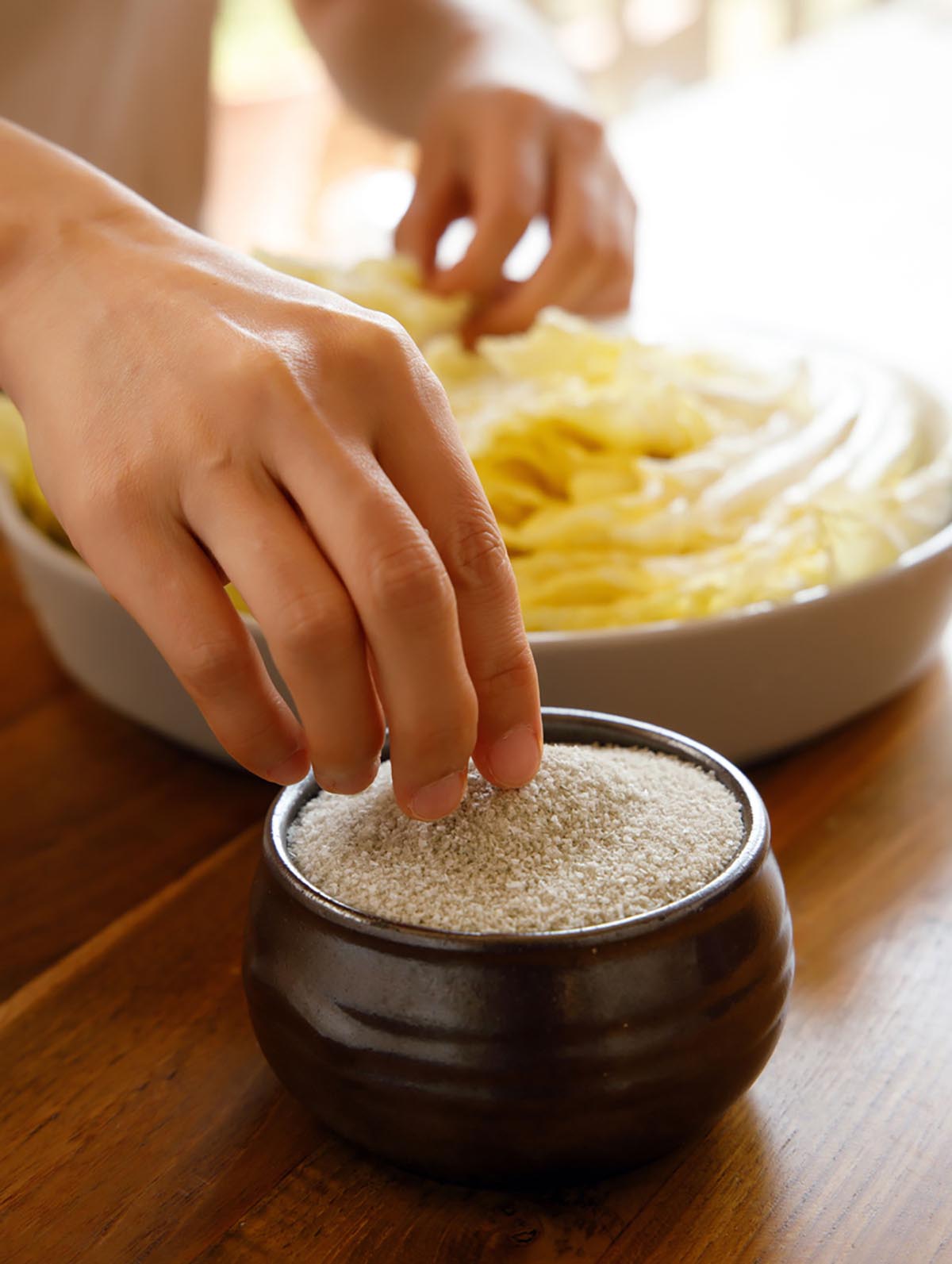 그릇에 소금이 수북히 담아져 있고, 노란배추속에 소금을 넣을려고 손으로 소금을 집고 있다.