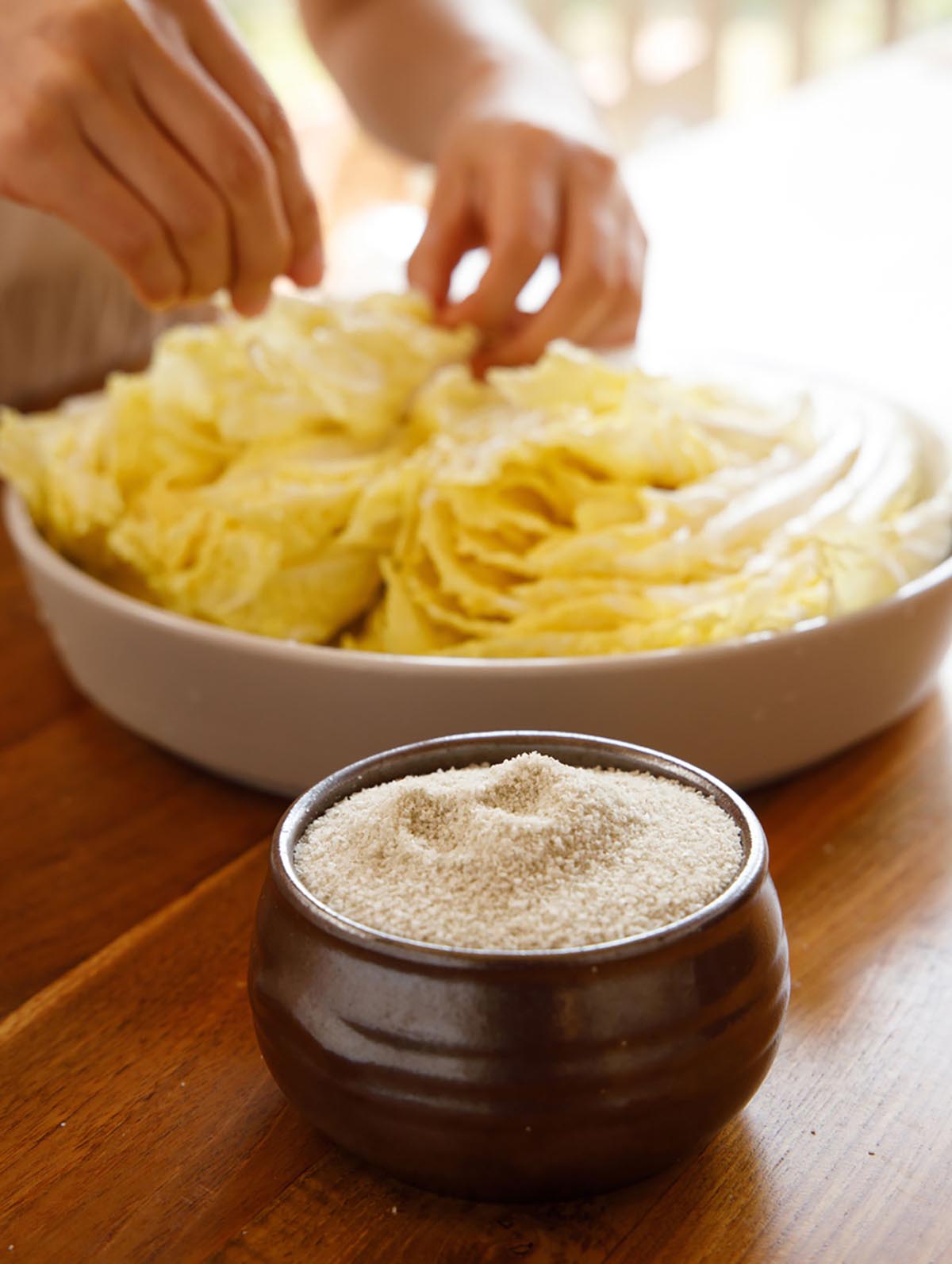 그릇에 소금이 수북히 담아져 있고,그 뒤로는 노란배추를 소금으로 절이는 모습이 있다.