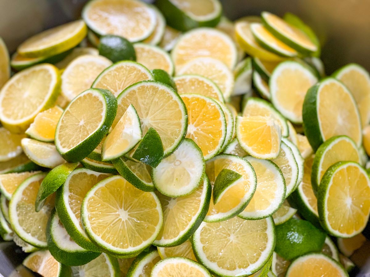 건조과일 과일칩을 만들기 위해 청귤을 얇게 동그랗게 썰어 초록 껍질과 노란 과육 단면이 보이게 겹겹이 쌓여 큰 통 안을 가득 채운 모습