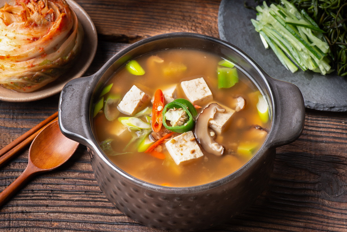 두부, 채소, 고추가 들어간 구수한 된장찌개가 검은 뚝배기에 담겨 있고, 국물에 된장의 깊은 맛이 배어 있다. 찌개된장으로 활용되는 클로렐라 된장의 용도 예시를 보여준다.