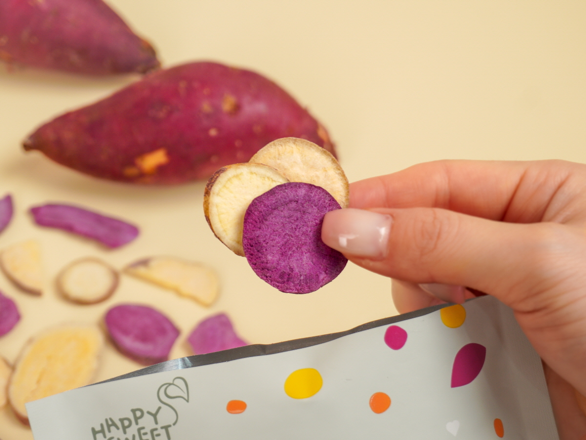 동글동글한 고구마칩을 꺼내서 손바닥에 올려놓은 모습, 대부분 하얀색 고구마칩이고 간간히 보라색이 보인다.
