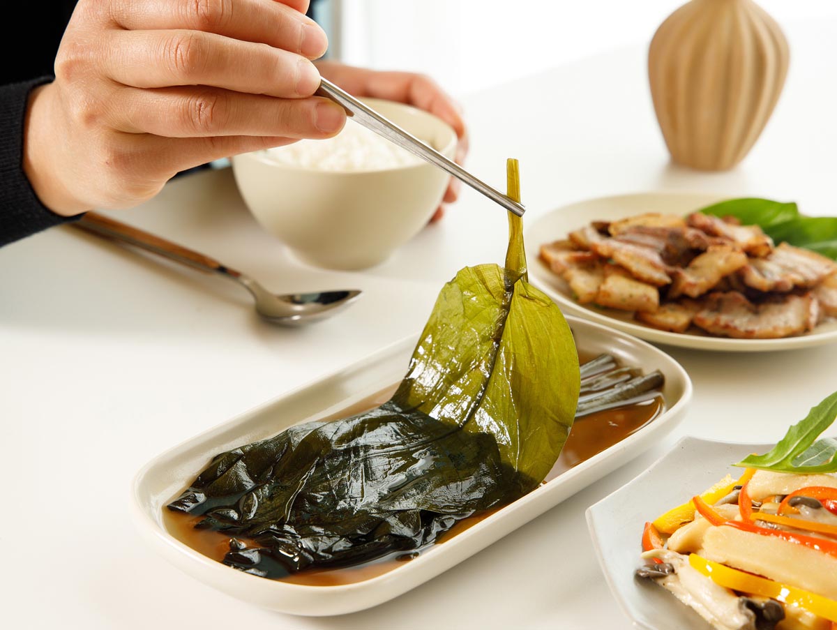 산마늘로 장아찌를 접시에 담아 삼겹살 구이와 함께 밥상을 차린 모습. 젓가락으로 한잎을 집어올리는 장면을 찍음 