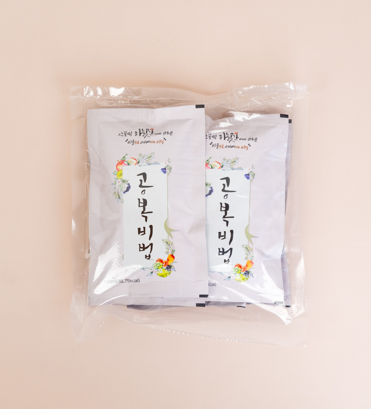 흰 식탁 위, 중앙에는 둥근 유리잔에 주황빛 액체가 담겨 있고 그 주변을 원재료인 과채들이 둥글게 둘러싸고 있습니다. 좌측 하단부터 검고 작은 아로니아 알갱이들, 주황빛 당근, 붉은 사과, 초록 풋사과, 초록빛 새싹보리, 연두빛 양배추, 초록빛 브로콜리, 붉은 토마토가 놓여있습니다.