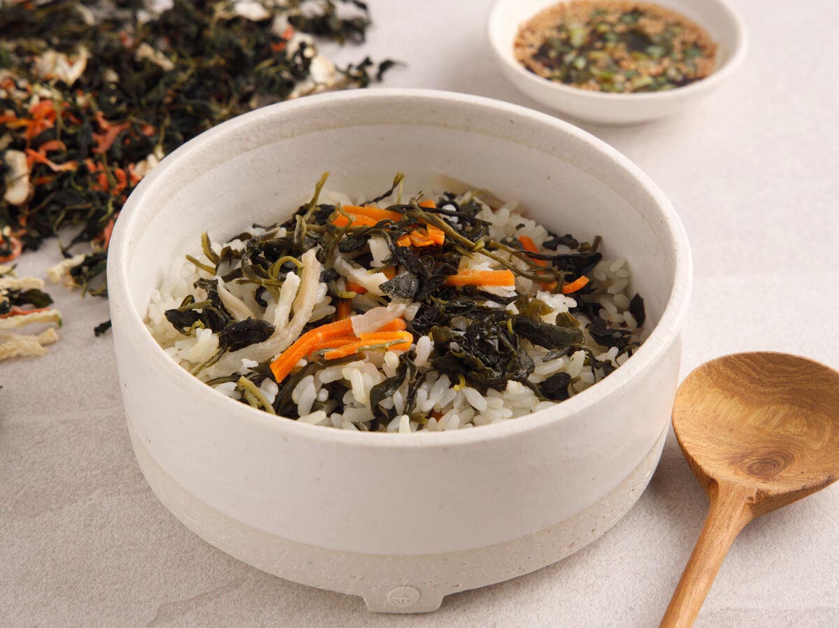 당근, 야채, 인삼,쑥부쟁이나물을 넣고 만든 인삼비빔밥이 하얀 그릇에 담아져 있고, 그 옆에는 나무수저가 놓여져 있다. 