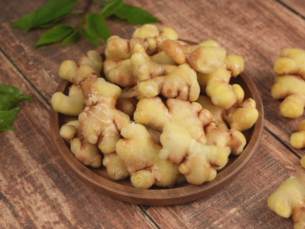 원목 쟁반 위에 생강청과 생강차 두 잔을 담고, 생강 뿌리와 허브잎을 함께 배치한 차세팅. 생강차활용 아이디어를 제시하는 구성.